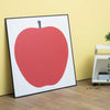 uno la mela art print in a black frame, placed on the floor leaning against a yellow painted wall